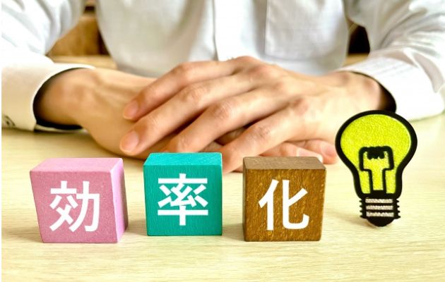 カラフルな積み木に「効率化」と書かれており、男性の手の前にカラフルな文字が書かれた積み木が置いてある写真