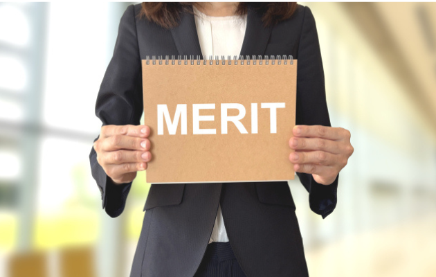 女性ビジネスマンがノートを持っている写真。ノートの表紙に「MERIT」と書かれている。