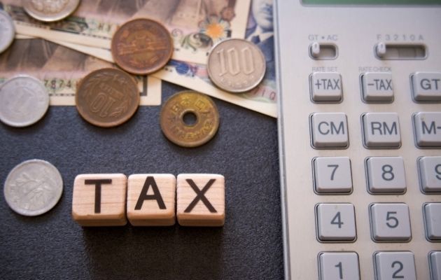 小さい積み木に「TAX」と書かれており、現金と電卓が一緒に写っている写真