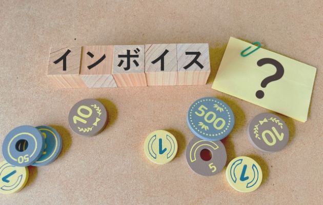 積み木に「インボイス」と書かれており、周りにはクエッションマークが書かれている付箋と現金のおもちゃが置いてある写真