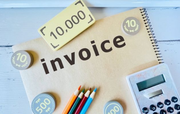 ノートの表示に「invoice」と書いてあり、電卓や色鉛筆、現金のおもちゃが置いてある写真