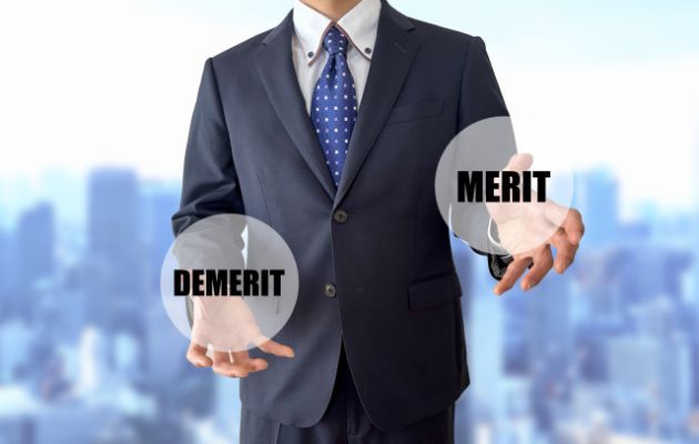 ビジネスマンが両手に「MERIT」と「DEMERIT」と書かれたものを持っている写真