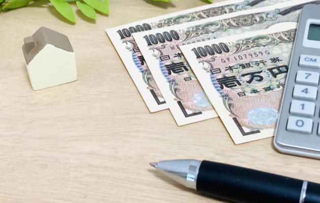 小さな家のおもちゃと現金、電卓、ボールペンが置いてある写真
