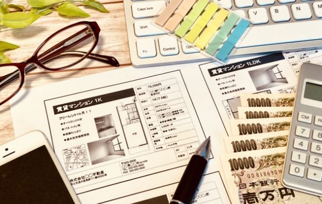 賃貸の案内書類と現金、電卓、キーボード、メガネ、スマートフォン、付箋が置いてあり、向いてる人と不要な人を表している写真
