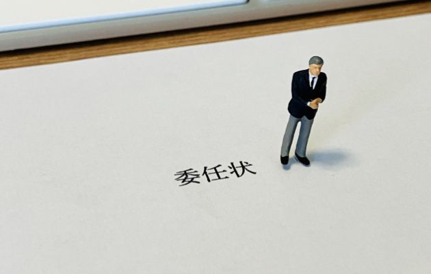 委任状と書かれた用紙にビジネスマンの男性の人形が置かれている写真