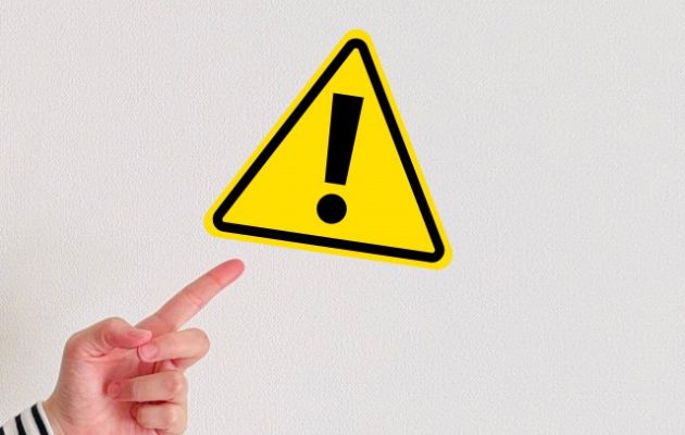 黄色い三角の中にびっくりマークが書かれていて、注意点を表している写真。注意マークを指で指している様子の写真。