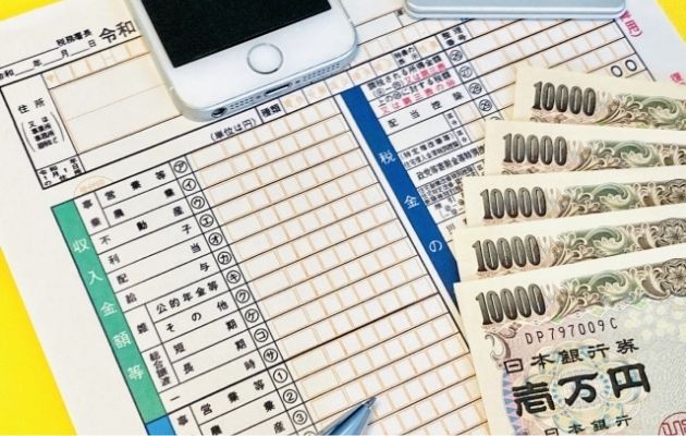 確定申告の書類と一万円の現金、スマホが置いてある写真