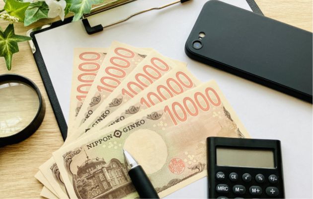 携帯、電卓、ボールペン、虫眼鏡、メモ紙と現金で相場を表している写真