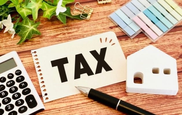破ったノート一枚に「TAX」と書いてある。周りに電卓、ボールペン、不動産の型、付箋、クリップが置いてある写真