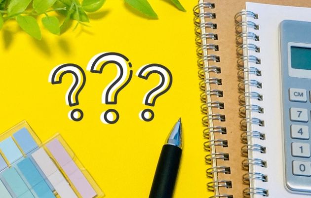 黄色い背景に、ノート、電卓、付箋、ボールペンが置いてあり、？？？マークが書いてある写真