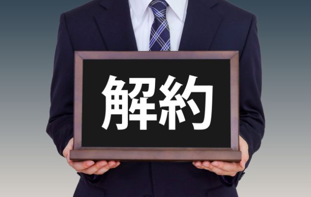 スーツを着た男性が胸元に「解約」と書いてある看板を持っている写真
