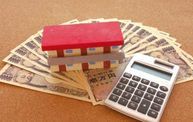 現金1万円が並んでいる上に不動産物件の模型と電卓がが置いてある写真