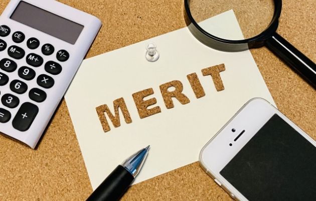 コルクボードに「MERIT」と書かれた用紙が貼られている。周りに電卓、虫眼鏡、スマートフォンが置いてある写真