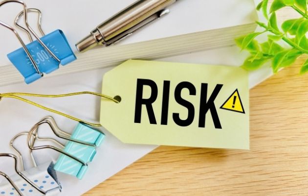 穴の空いたタグに「RISK」と黄色の三角にびっくりマークが書かれている。周りにはクリップとボールペンが置いてある写真