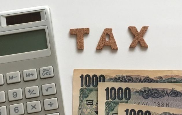 電卓と現金が置いてあり、そこに「TAX」と文字が並べられている。節税効果を表している写真