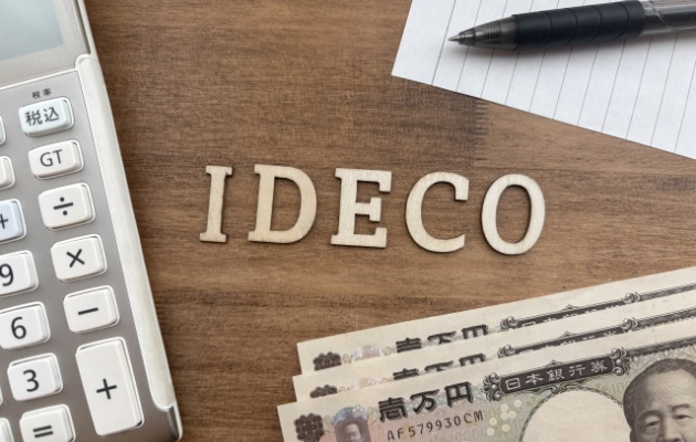 電卓、お札、メモ紙、ボールペンの置いてあるところに「IDECO」と木の文字型が置いてある写真