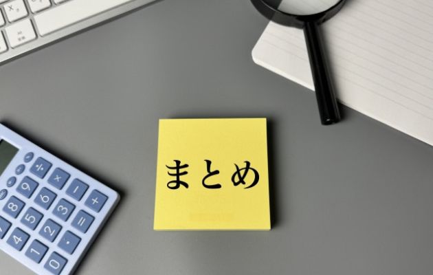 デスクに置いてある黄色い付箋に「まとめ」と書いてある。周りにはキーボード、電卓、虫眼鏡、ノートが置いてある写真