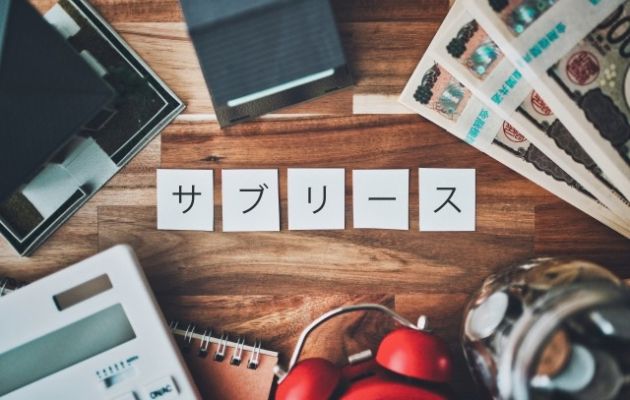 サブリースの言葉の周りに現金、電卓、時計、硬貨などが置いてある写真