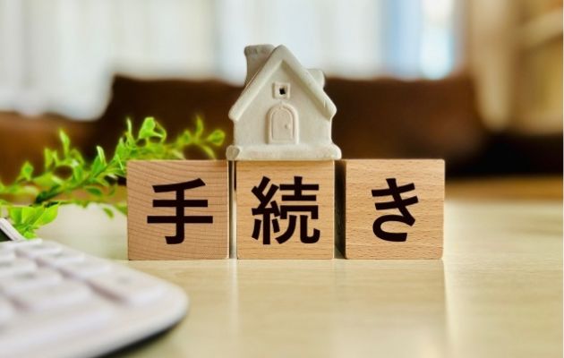木のブロックに「手続き」と書いてある。続の文字の上に家の物件模型が置いてある写真