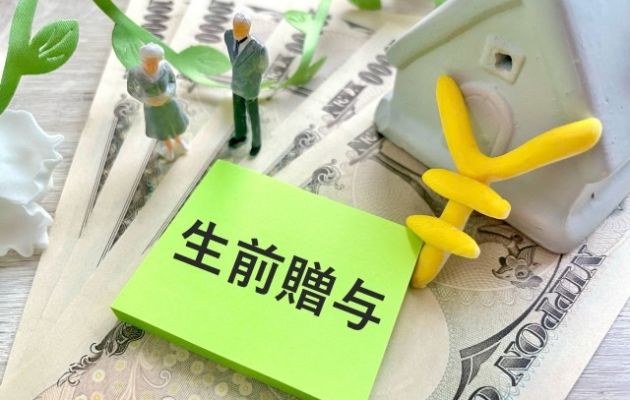現金と家の模型の上に、付箋がと老夫婦の人形が置いてあり、「生前贈与」と書かれている写真