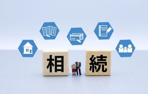 積み木に「相続」と書かれており、積み木の間に老夫婦がお辞儀している人形が置かれている写真