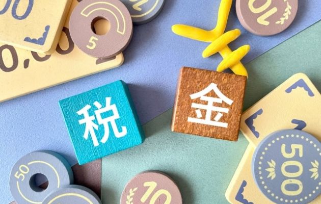 木のブロックに税金と書いてあり、おもちゃの現金と「￥」マークのおもちゃが置いてある写真