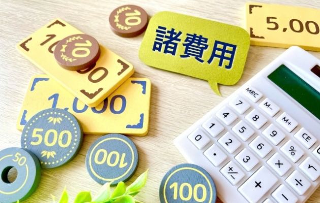 電卓とおもちゃの現金が置いてあり、電卓から吹き出しで「諸費用」と書かれた文字が出ている写真